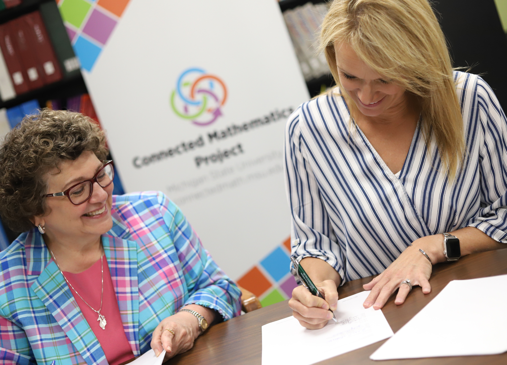 Anne Di Sante (left), Executive Director of MSU Technologies, and Lisa Kelp (right), VP of Learning and Development at Lab-Aids sign the partnership agreement for Lab-Aids to publish the next edition from Connected Mathematics Project at Michigan State University.